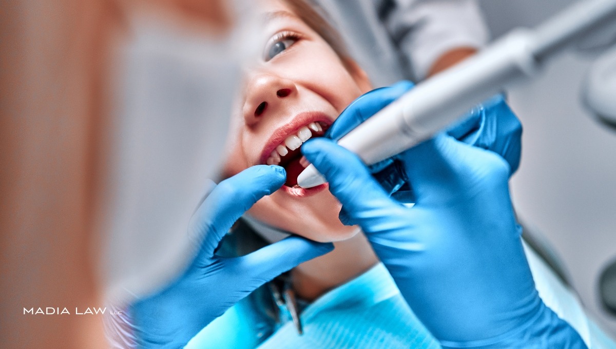 A close-up of a dentist in blue gloves performing a procedure on a young patient's teeth using a dental drill, illustrating a common scenario for dental negligence or injury claims.