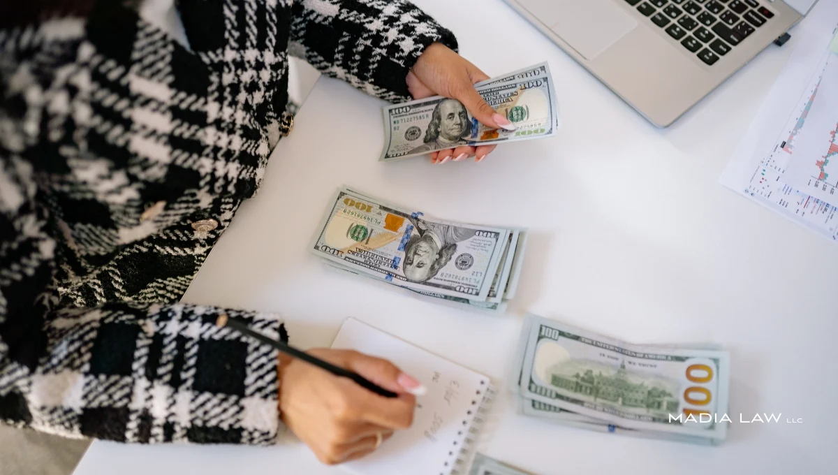 An employer counting cash and documenting figures in a notebook to determine the amount of a worker's wages to be garnished or withheld.